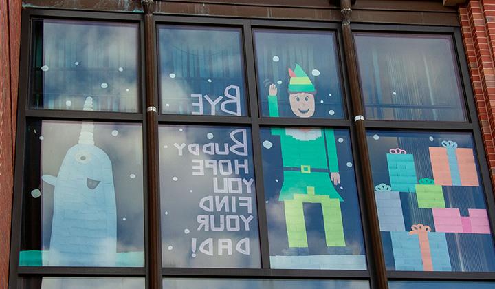 Res hall windows decorated in sticky notes to display Buddy the Elf and a narwal